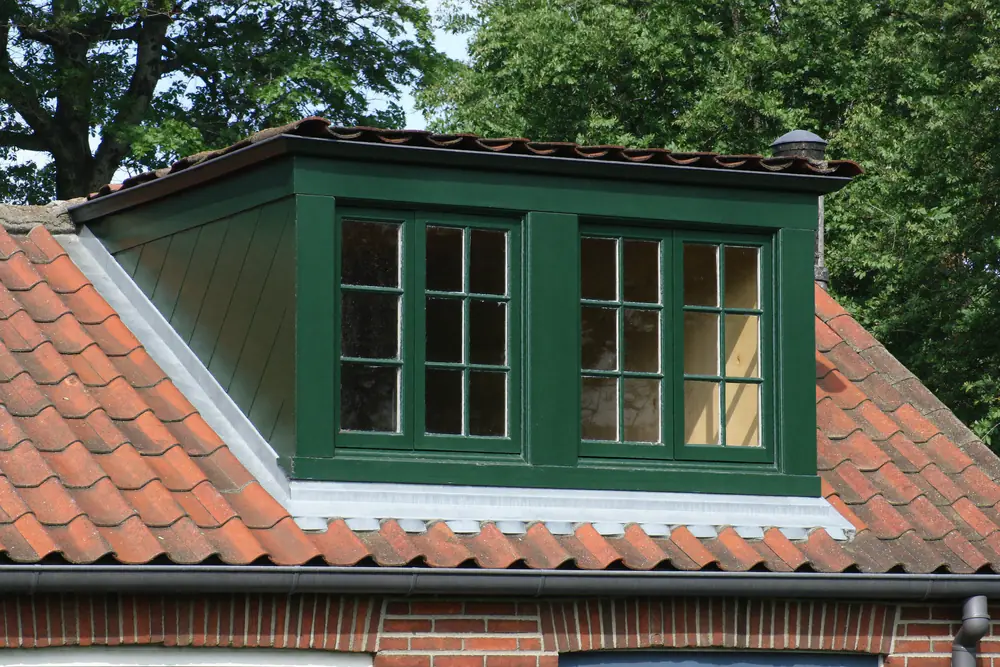 Donkergroen geschilderde houten dakkapel met roedeverdeling op een dak van een jaren 20 woning