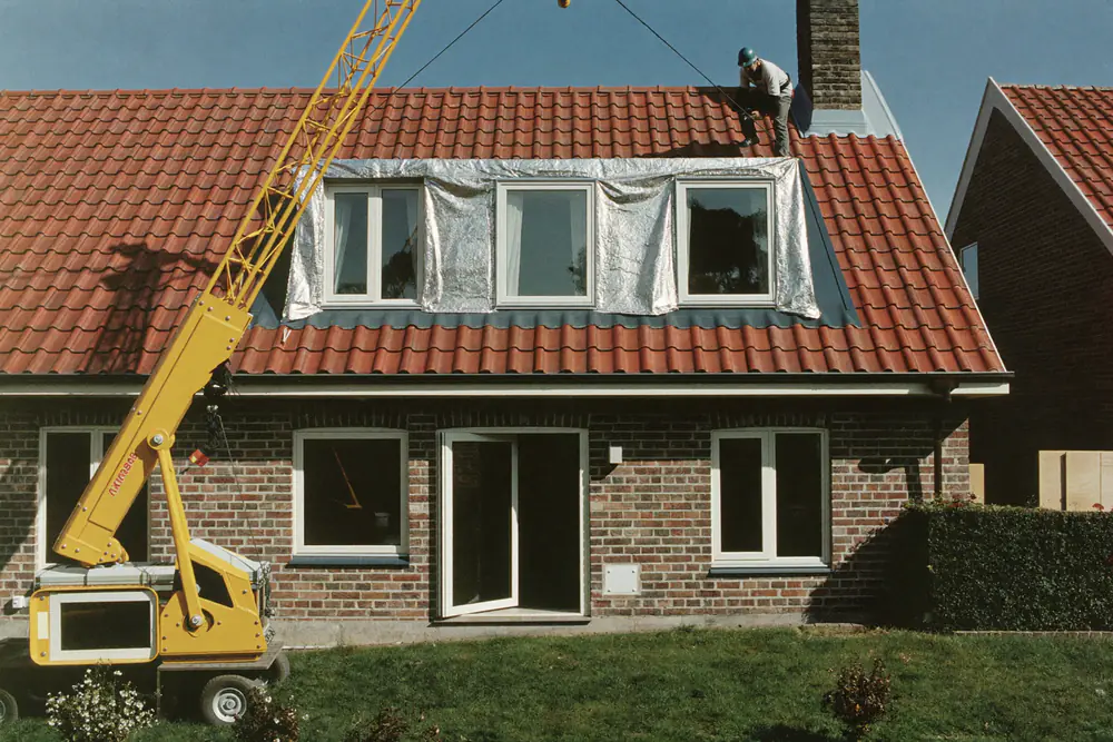 Een prefab dakkapel wordt met een kraan op het dak van een bakstenen woning geplaatst