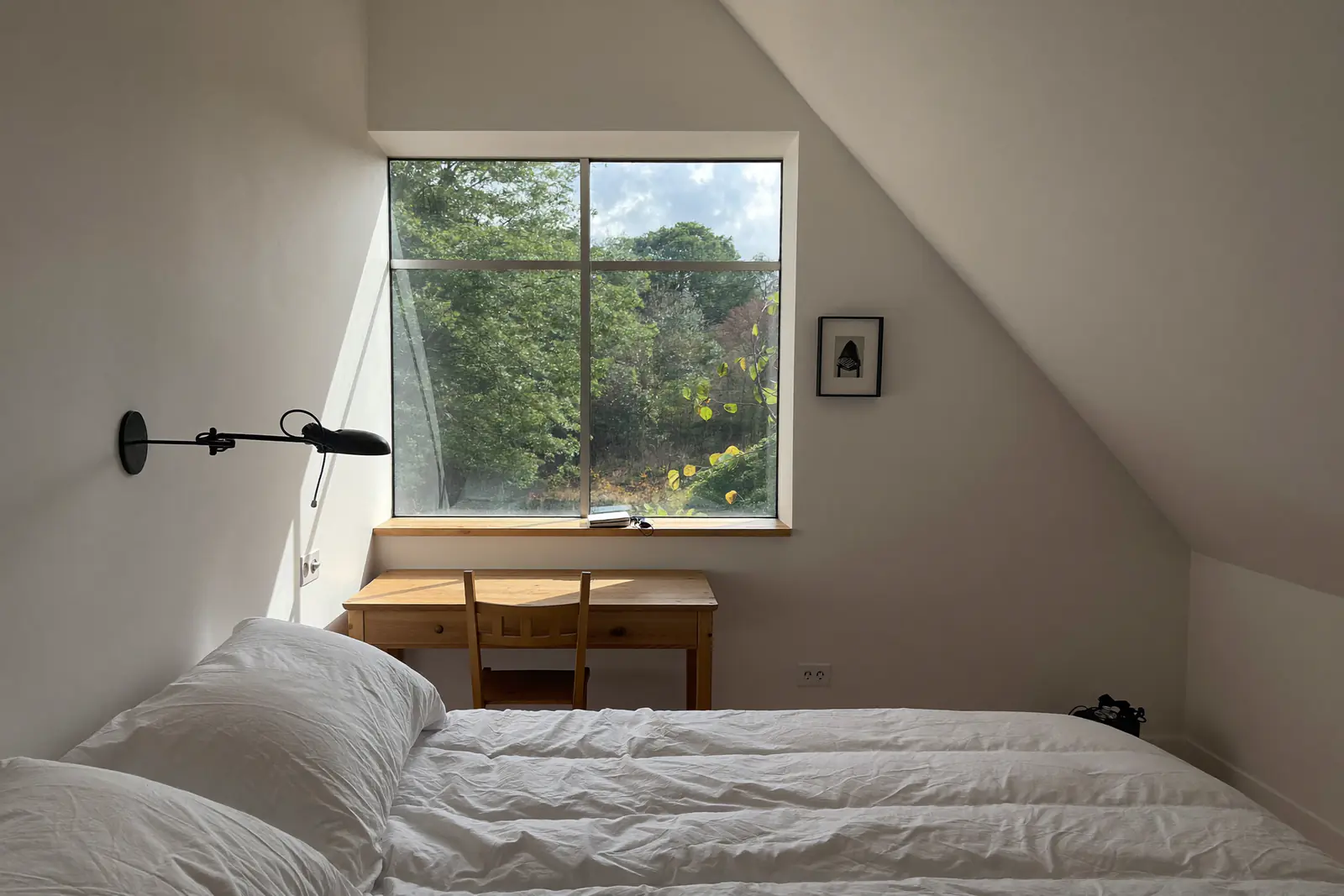 Lichte zolderkamer met een brede dakkapel, bed en bureau met uitzicht op de bomen